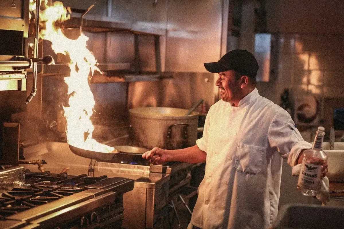 En cuisine, un chef fait sauter une poêle dans une flamme, en plein service.