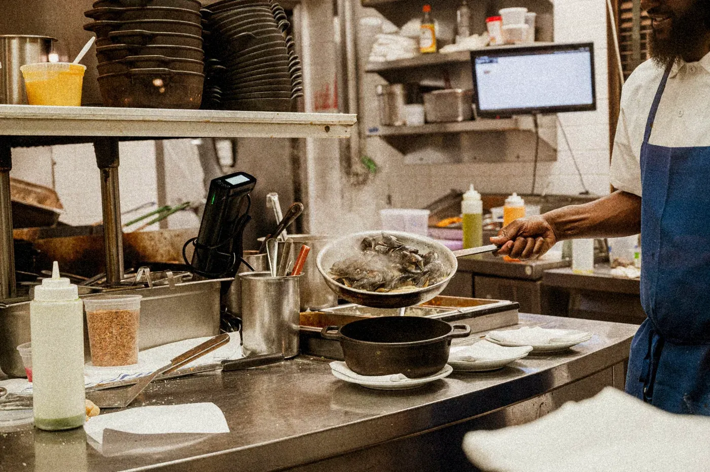 En plein service, un cuisinier fait sauter des moules fumantes au-dessus d’une cocotte en fonte.