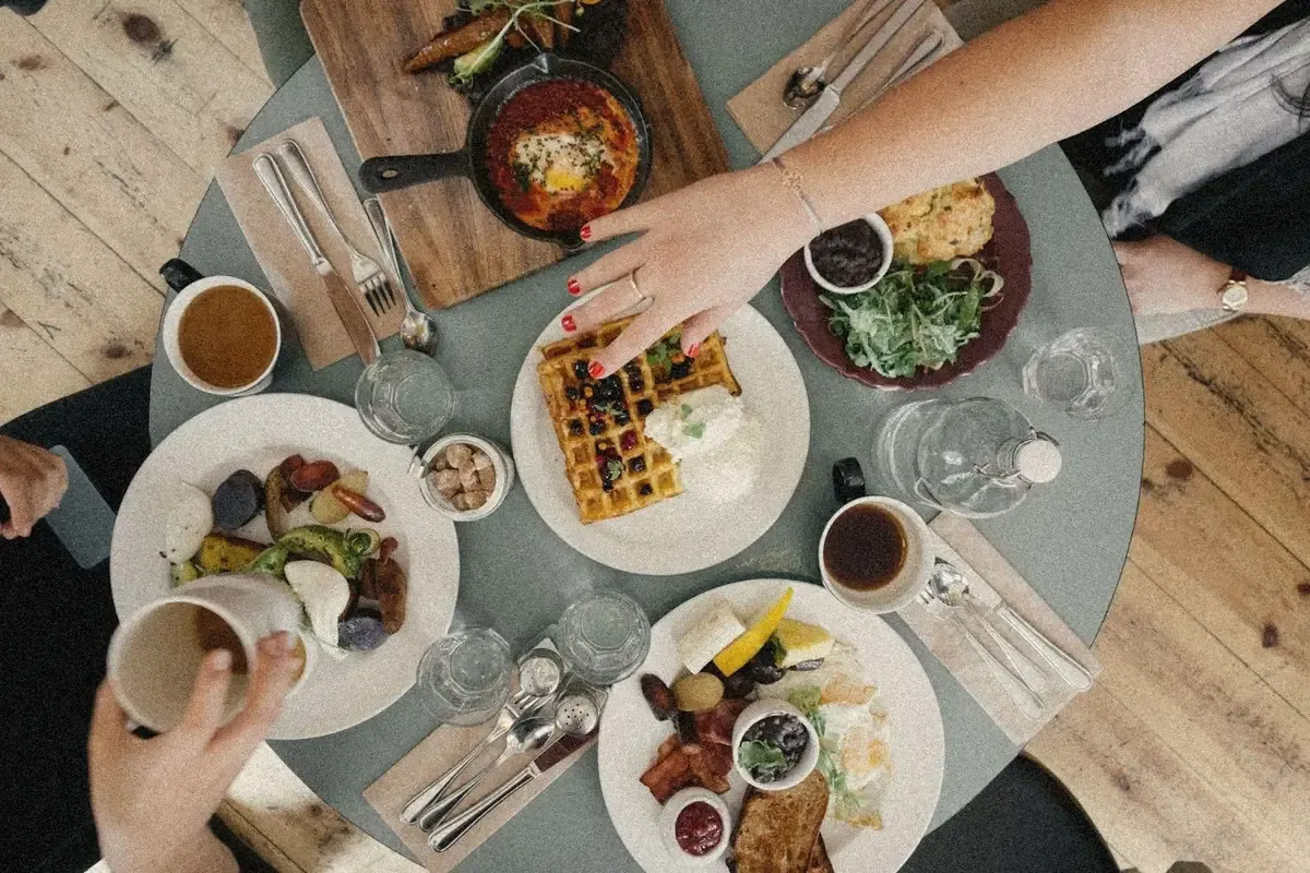 Vue du dessus d’une table partagée : des mains passent entre les assiettes et les tasses.